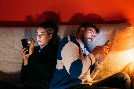 Two people sit next to each other and browse their phones to show how politics and dating in India have impacted how Indians are swiping on dating apps like Tinder basis different political ideologies dating
