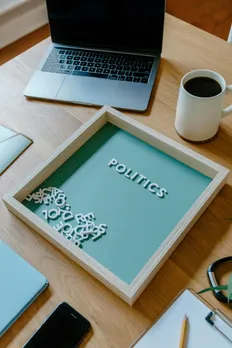 A zoomed out picture of a person's workspace, with a laptop, cup of coffee and a board that spells the word 'politics' to show how different political ideologies dating have come together and the importance of politics and dating in India.