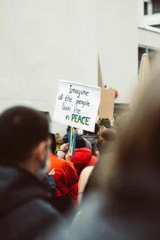 A zoomed out shot of a person at a protest holding a sign asking for peace to signify politics and relationships in India and the importance of political compatibility in relationships.