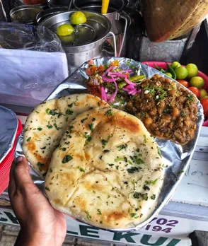 A picture of a plate of chole kulche against the backdrop of a stall serving the must-try Indian street food, to depict how it's acquired the one of best street food India status.