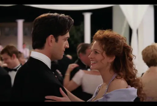 A man dances with a woman while at a wedding, to depict the original gay best friend trope in Hollywood, while also showing straight women and gay men friendship