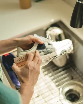 A man scrubbing his sneakers with a white shoe cleaner brush