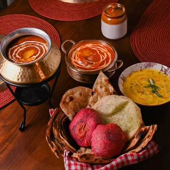 A picture of a table full of food-dal, butter chicken, breads and achaar to show how Punjabi cuisine in India comprises dishes that aren't a part of Punjabi food history, making one question Punjabi cuisine authenticity