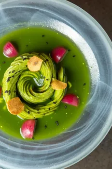A picture of an artfully placed green swirl atop a green sauce and red cherry tomatoes to show how luxury vegetarian dining India and upscale vegetarian restaurants India are serving the best via their tasting menus