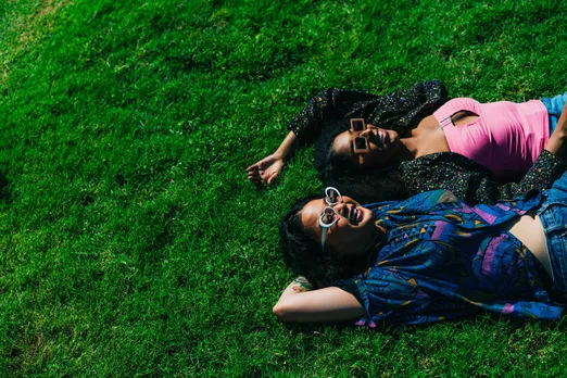A picture of two women laying down on the grass and talking to each other to show how queer dating in India leads to staying friends with exes in the LGBTQ community India