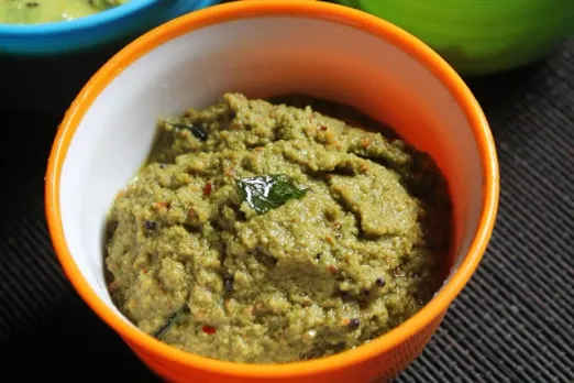 A picture of a bowl of green and yellow condiments with ingredients around it to show how Indian condiments are a form of sustainable practice