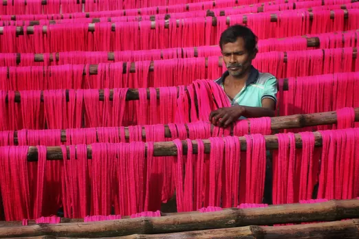 A picture of a man working with pink weaves to show how the immigration paradox within India's textile industry to highlight the root of anti immigration protests