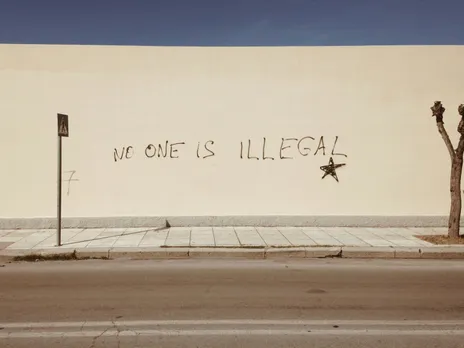 A picture of a yellow wall with the words 'no one is illegal' drawn on it to depict the anti immigration protests which also involves Indian immigrants