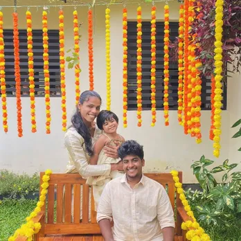 A picture of a man and a woman with a child in front of a house decked up for festivities to depict the rise of LGBTQ+ families in India and queer parenting in India