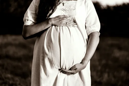 A sepia picture of a woman wearing a white dress holding her baby bump with her arms to show how despite harsh surrogacy laws for queer couples India, queer parenting in India is evolving