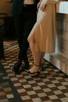 A picture of the lower halves of a couple-a woman in heels and a dress with a slit and a man wearing shoes and pants, belt, shirt and a coat-to depict now making the effort or knowing how to plan a first date as one of the primary first date red flags that people tend to overlook due to the current dating app culture India