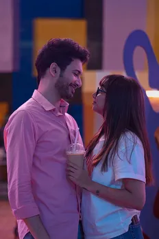 A picture of a man in  pink shirt and a woman in specs holding a takeaway cold coffee to depict the meet cute scene in the Indian show Mismatched to show how first impressions in dating have evolved given the way people pick partner has changed thanks to dating app culture India, which has also impacted the concept of stereotypes and first impressions