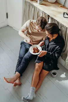 A couple sitting on the floor and kitchen and enjoying pancakes from the same plate while having a chat