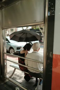 An old couple sitting outside a café; the man holds an umbrella on the woman's head