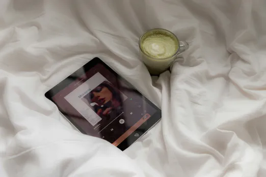 A picture of an I-pad and a cup of matcha latte on a bed with white sheets
