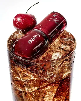 A red lip tint from Korean makeup brand Fwee, placed on a glass of cola