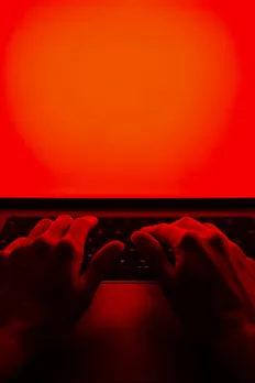 A picture of a person's hands on a laptop with a red screen in red light to show how rage baiting in marketing works due to the rise of social media outrage