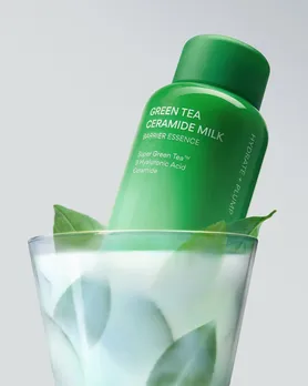 A green colour bottle of milky toner placed in a glass of white milky liquid