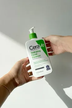 A white and green bottle of CeraVe non foaming cleanser in a woman's hand
