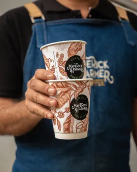 A picture of a man holding two take away cups of coffee from Maverick and Farmer, one of the luxury coffee brands in India that's considered premium coffee India