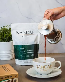A picture of coffee being poured into a cup with a packet of Nandan Coffee, which offers freshly roasted coffee India, besides being a Indian single-origin coffee. A brand that has been instrumental in the growing popularity of luxury coffee brands in India