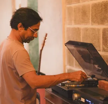 A man places the needle of a vinyl record player on a record to show how vinyl record players India and vinyl records in India are gaining popularity via vinyl listening rooms India and vinyl cafe India like Vinyl and Brew India