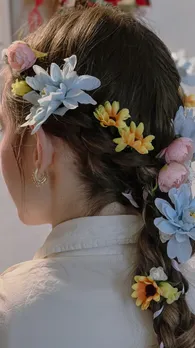 A back shot of a woman's hair braided with powder blue, yellow and pink flowers on it.