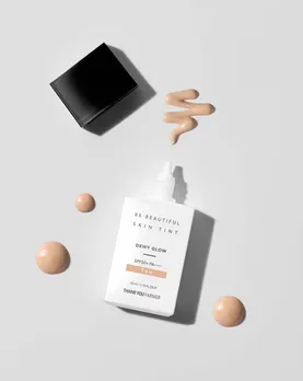 A bottle of a skin tint placed on a table with some product oozing out