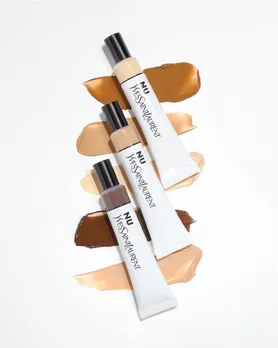 A flatlay shot of tubes of YSL skin tint placed on texture swatches of the skin tint against a white background