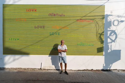 1. Munir Kabani against the backdrop of his mural on Arthshila wall, Fort Kochi