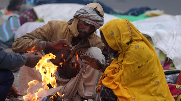 People sit around a bonfire at a roadside on a cold winter morning during fog, in New Delhi