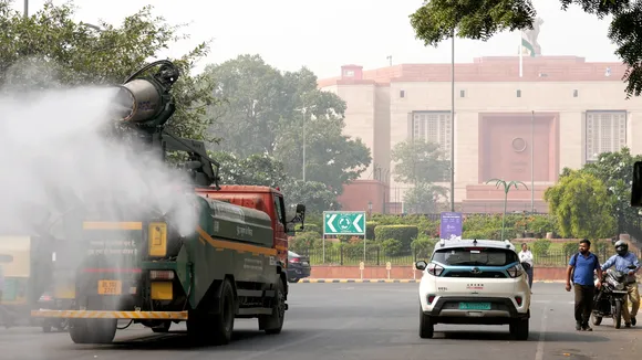 Commuters move past an anti-smog gun spraying water to curb air pollution near the Parliament House, in New Delhi, Saturday, Nov. 9, 2024