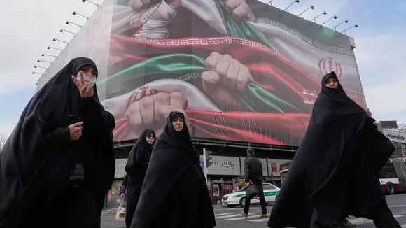 Women cross a street under a huge banner showing hands firmly holding Iranian flags as a sign of patriotism, as one of them flashes the victory sign, in Tehran, Iran, Wednesday, Jan. 14, 2026. (AP/PTI Photo)