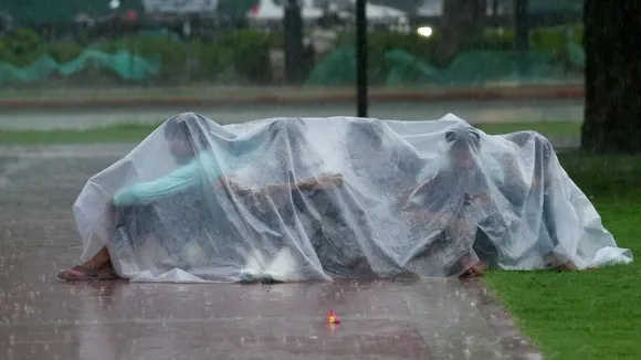 People take cover under a plastic sheet during rain, in New Delhi, Sunday, Aug. 11, 2024