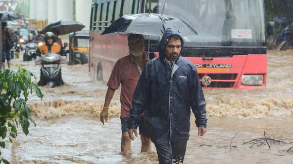 Pedestrians and vehicles move through a waterlogged road during rains, in Thane, Thursday, July 25, 2024.
