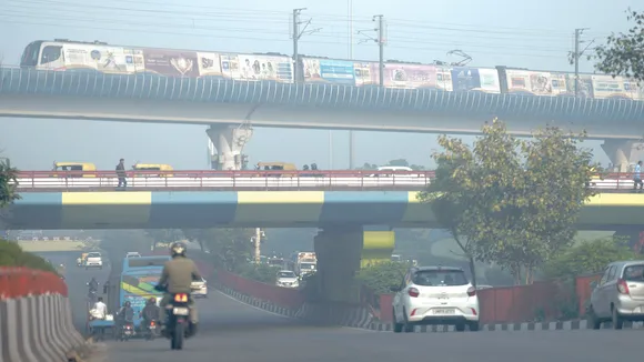 A metro train runs on its track as vehicles ply on a road amid smog, at Dhaula Kuan in New Delhi