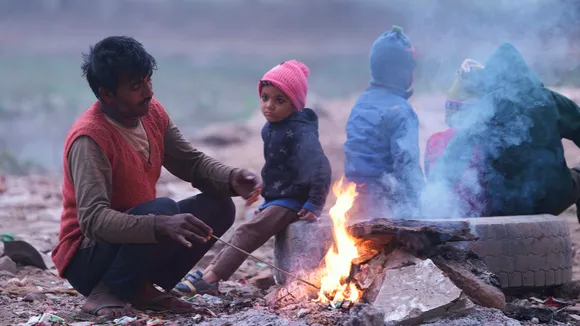 A man and children sit around a bonfire during fog on a cold winter morning, in New Delhi