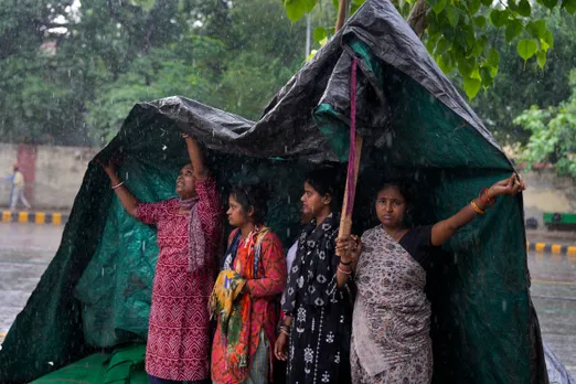 People cover themselves with a plastic sheet during rain at Jantar Mantar, in New Delhi
