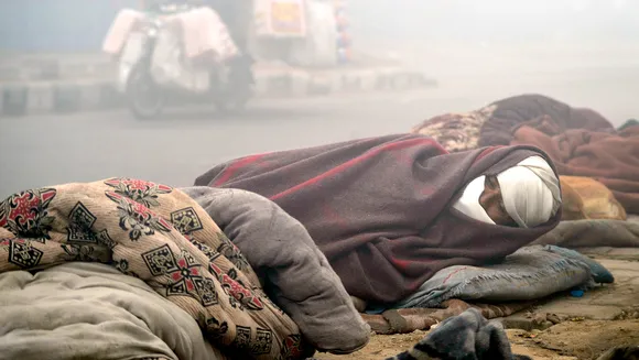 A homeless man wrapped in a blanket sleeps on the pavement on a cold winter day