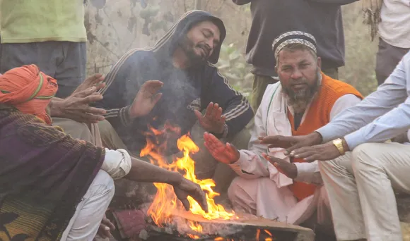 People sit near a bonfire to warm themselves on a cold winter morning, in Gurugram