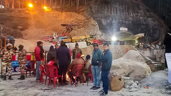 Security and media personnel gather around a bonfire during the rescue operation of 41 workers trapped inside the Silkyara tunnel, in Uttarkashi, Thursday, Nov. 23, 2023.