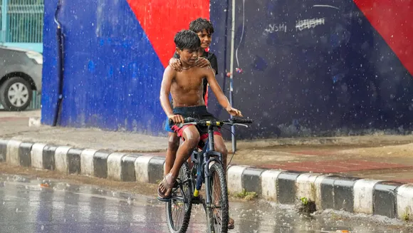 Young men ride a bicycle during rain, in New Delhi, Wednesday, May 29, 2024