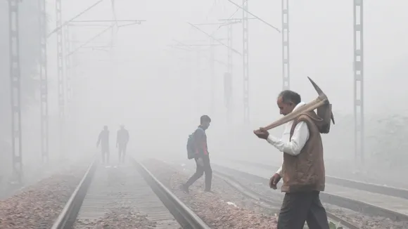 Commuters cross a railway track amid fog on a cold winter morning
