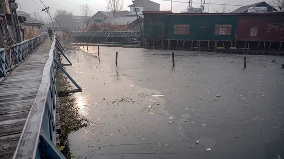 A man walks on a wooden bridge over the partially frozen interior part of Dal Lake during a cold winter morning as intense cold wave grips Kashmir valley