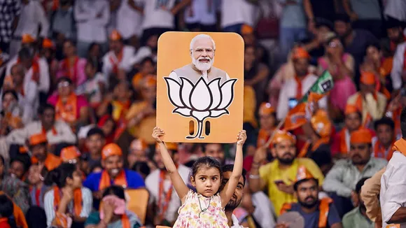 A child holds a placard depicting PM Modi and BJP election symbol during a public meeting addressed by Uttar Pradesh Chief Minister Yogi Adityanath for Lok Sabha polls, in Varanasi, Saturday, May 25, 2024