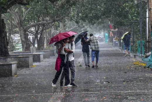 People walk past covering themselves under an umbrella during rainfall as monsoon arrives in Kerala