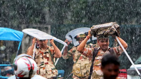 Security personnel shield themselves from rainwater, in New Delhi, Sunday, Aug. 11, 2024.