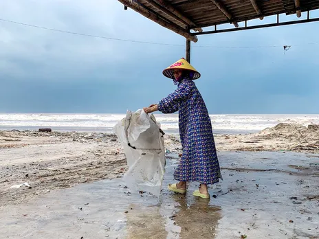 A woman wearing a raincoat collects a plastic bag near a beach as Typhoon Bualoi nears (Photo/ Reuters)