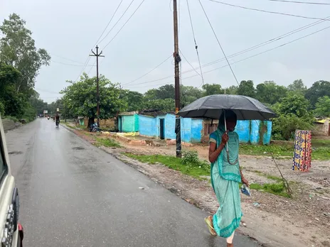 वर्षा से बचाव को छाता लगाकर जाती महिला