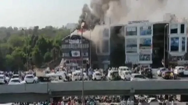 ସୁରଟର ଏକ ଟ୍ରେନିଂ ସେଣ୍ଟରରେ ଭୟଙ୍କର ଅଗ୍ନିକାଣ୍ଡ । ଜୀବନ ବଞ୍ଚାଇବାକୁ ଯାଇ ୪ ମହଲା ଛାତରୁ ଡେଇଁପଡି ଜୀବନ ହାରିଲେ ୧୫ ଛାତ୍ରଛାତ୍ରୀ । ଦେଖନ୍ତୁ ସେହି ସମୟର ଭିଡିଓ ।